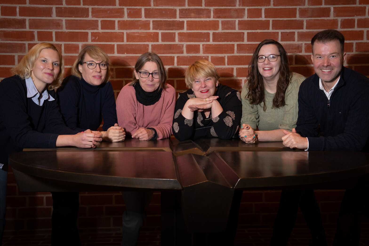 Eine Gruppe Menschen steht an einem Tisch und lächelt in die Kamera.