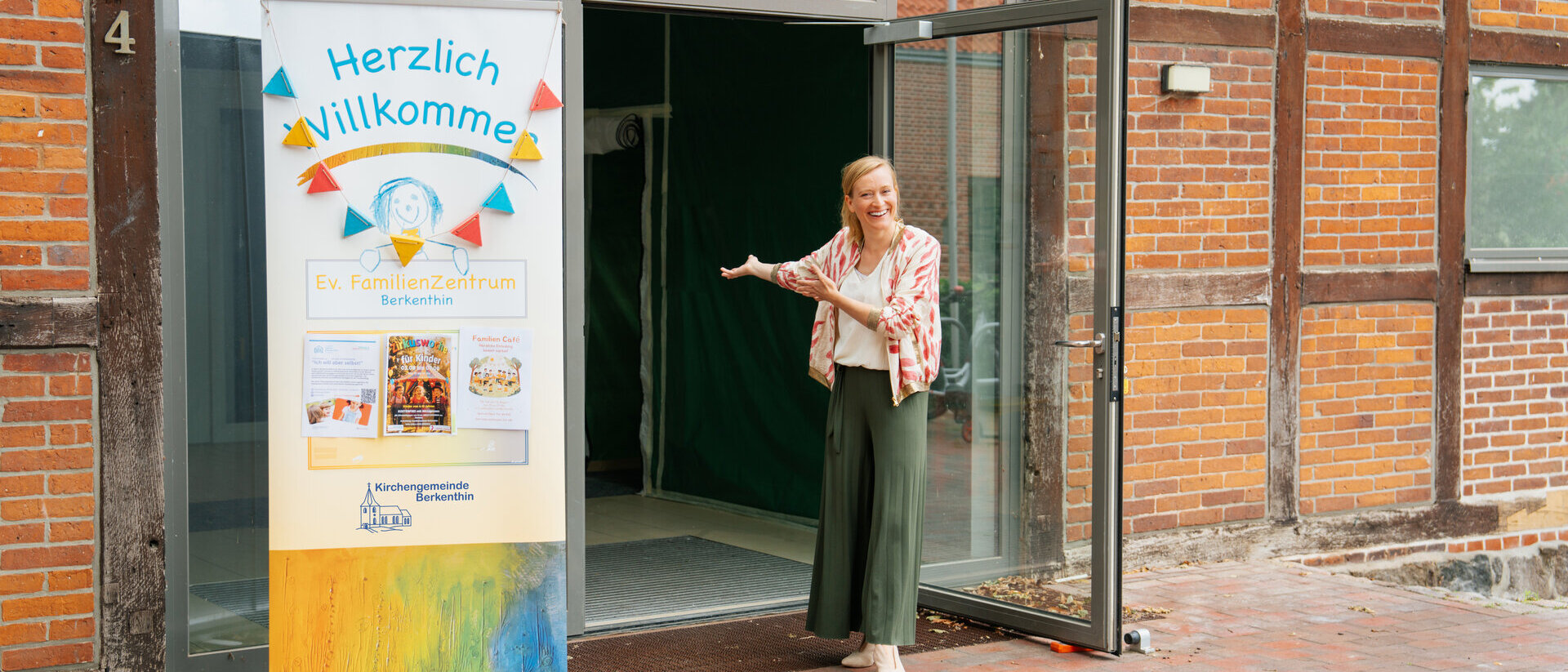 Imke Köhn steht in einladender Pose vor der offenen Glastür des Familienzentrums.